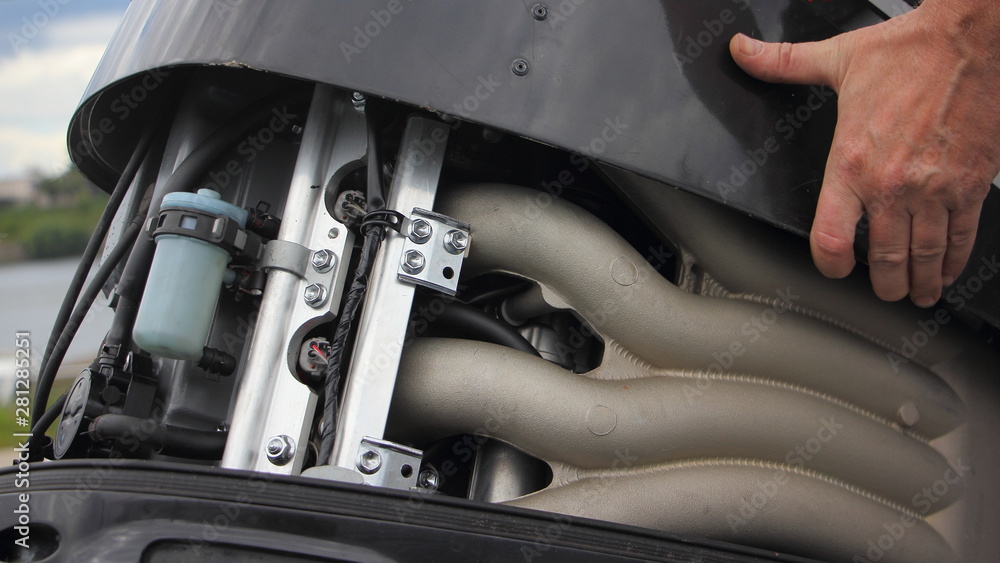 A man's hand open the hood of a powerful boat outboard motor, repair