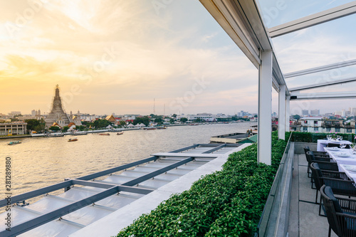 Photography Renovated Wat Arun (The Temple of Dawn) with boats moving over Chaophraya river that view from modern restaurant in the evening in Bangkok, Thailand