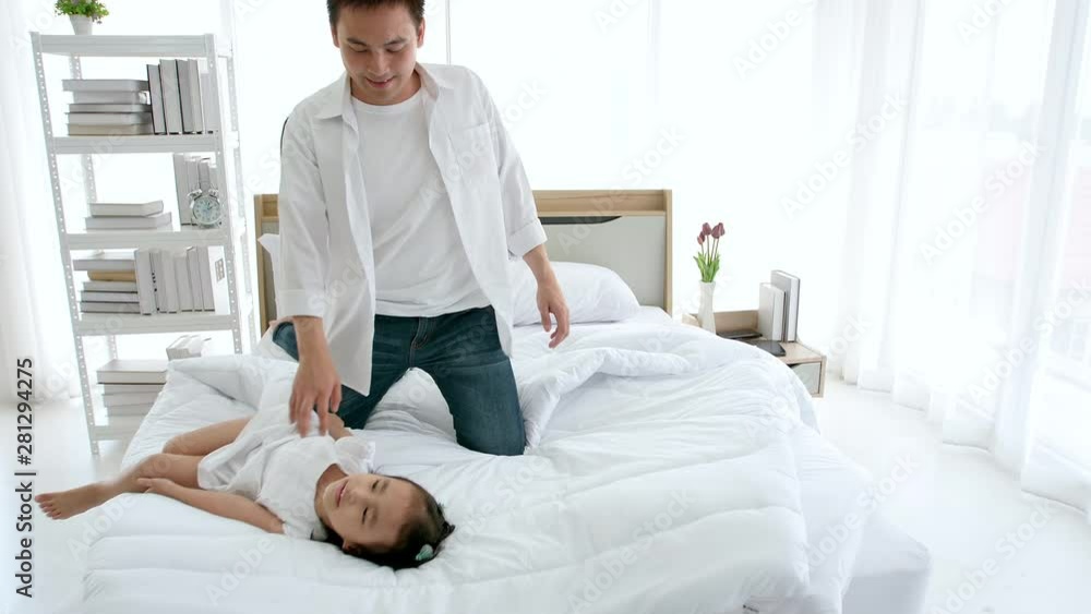 Asian family happy spending time together in the house. Father, mother and daughter, aged three enjoying playing on the bed. Asian family happy spending time together in the house. Father, mother and daughter, aged three enjoying playing on the bed.