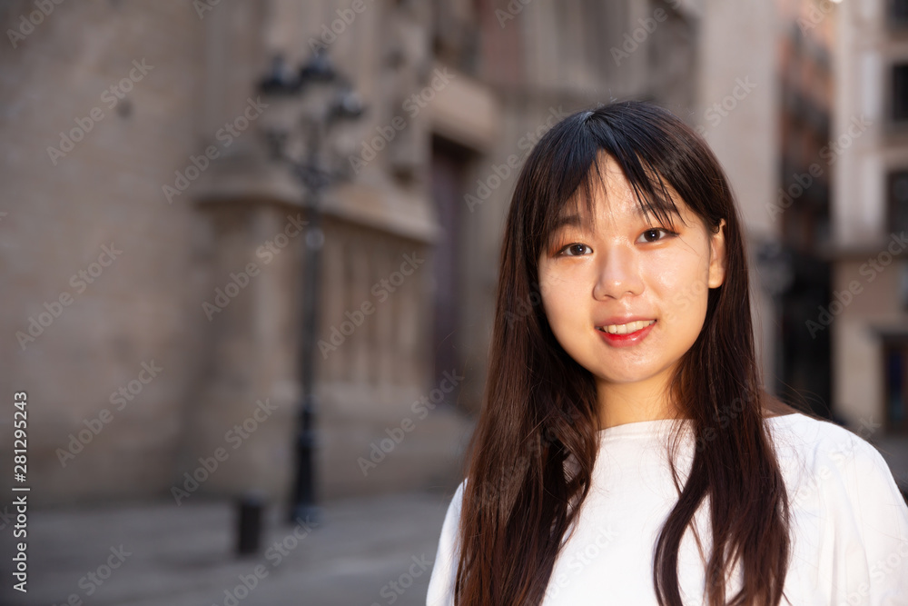 Fototapeta premium Portrait of cheerful young chinese longhaired woman standing on a city street