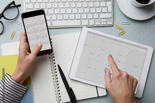 Top view of woman holding smartphone and tablet with calendar on desk photo
