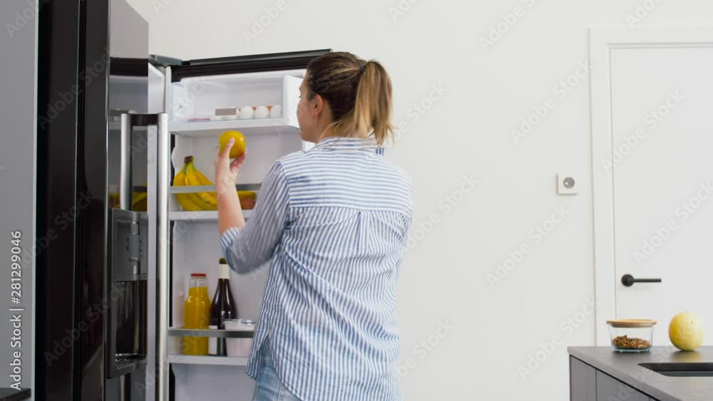 healthy eating, food and diet concept - happy woman opening fridge and taking apple at home kitchen healthy eating, food and diet concept - happy woman opening fridge and taking apple at home kitchen