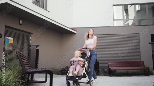  young mother walks with a little girl with her daughter in a baby carriage near the house