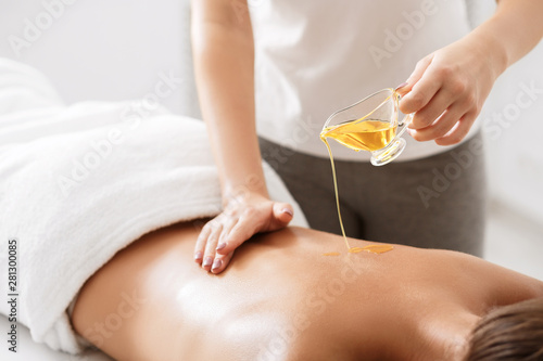 Masseur pouring aroma oil on female back