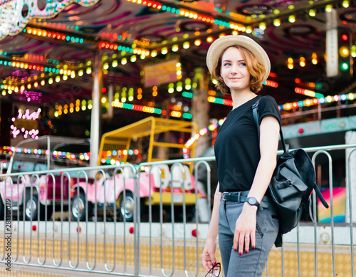 Fotografering Young cheerful hipster woman in glasses and hat in amusement park