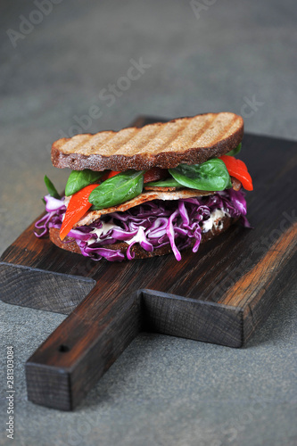 Sandwich with meat, red cabbage, spinach and grilled red pepper. Close-up. Dark background.  Vertical orientation of the frame.