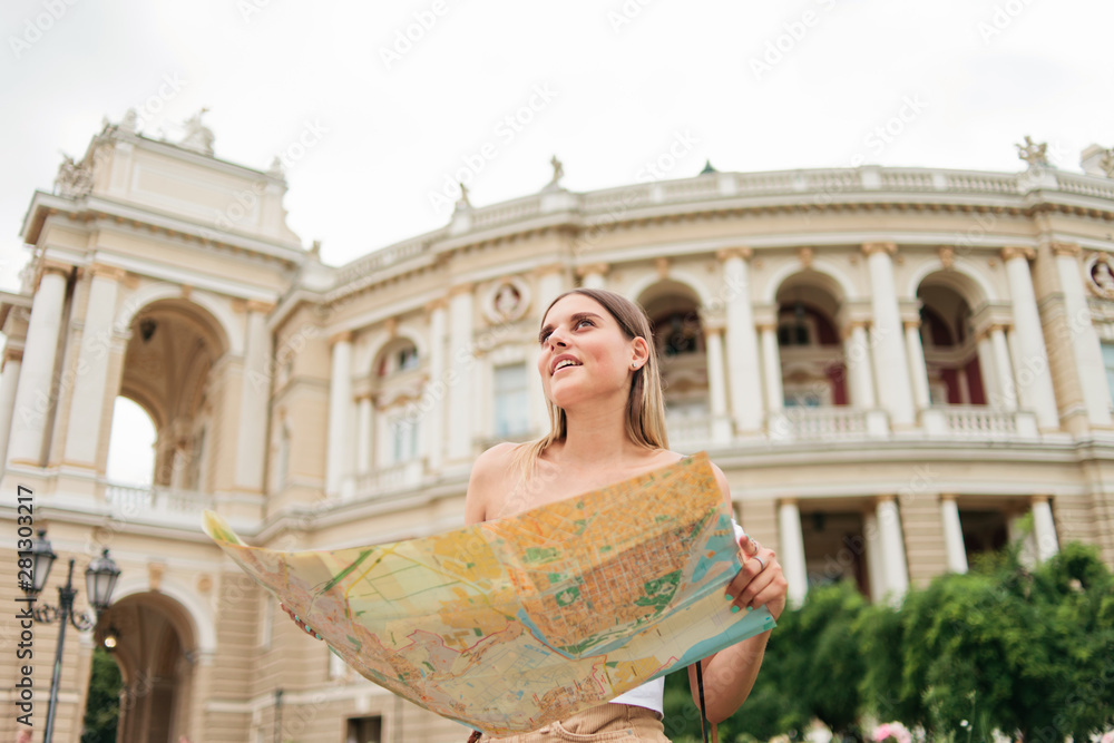 Young, charismatic woman tourist holds in her hands map of the city against the background of the architecture of a tourist city. Traveling to new places