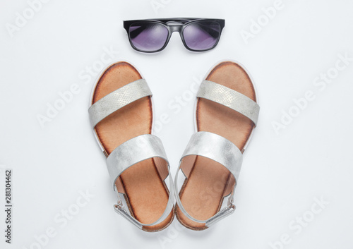 Stylish female sandals and sunglasses on white background. Top view