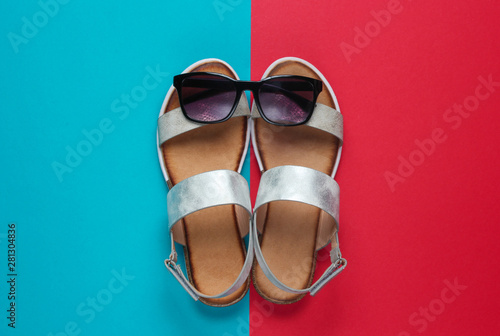Creative summer beach flat lay. Leather women's sandals, sunglasses on blue red background. Top view
