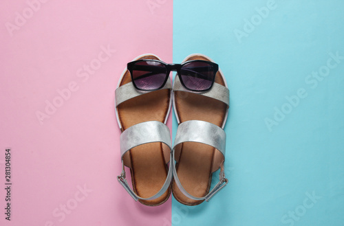 Creative summer beach flat lay. Leather women's sandals, sunglasses on blue pink background. Top view
