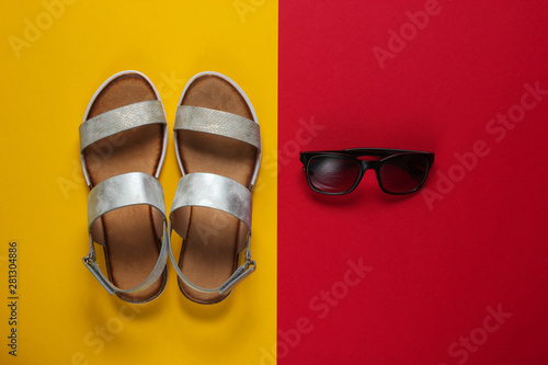 Creative summer beach flat lay. Leather women's sandals, sunglasses on yellow red background. Top view