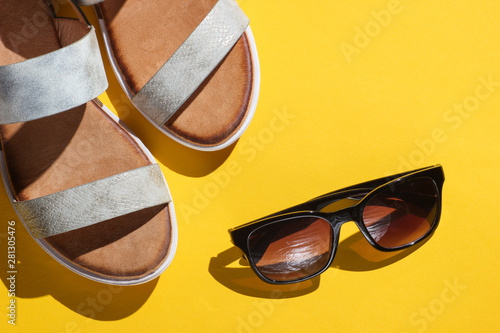 Fashionable women's sandals with sunglasses on a yellow background. Summer accessories