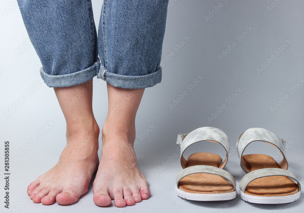 female bare feet in jeans and sandals on a white background. Studio fashion shot. Crop photo female bare feet in jeans and sandals on a white background. Studio fashion shot. Crop photo