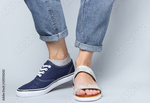 Female legs in jeans shod in sneaker and sandal on white background. Seasonal shoes. Creative fashion shot