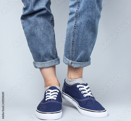 Fashion studio shot. Female legs in jeans and sneakers on a gray background.