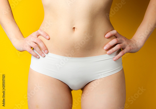 Beauty studio shot. Female slim body in white panties on yellow background