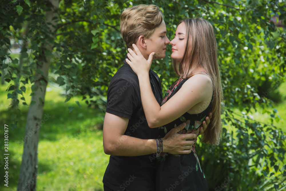 A couple of teenagers in love hugs and poses against the background of flowering trees and shrubs. Young guy and girl on the background of a blooming Park A couple of teenagers in love hugs and poses against the background of flowering trees and shrubs. Young guy and girl on the background of a blooming Park