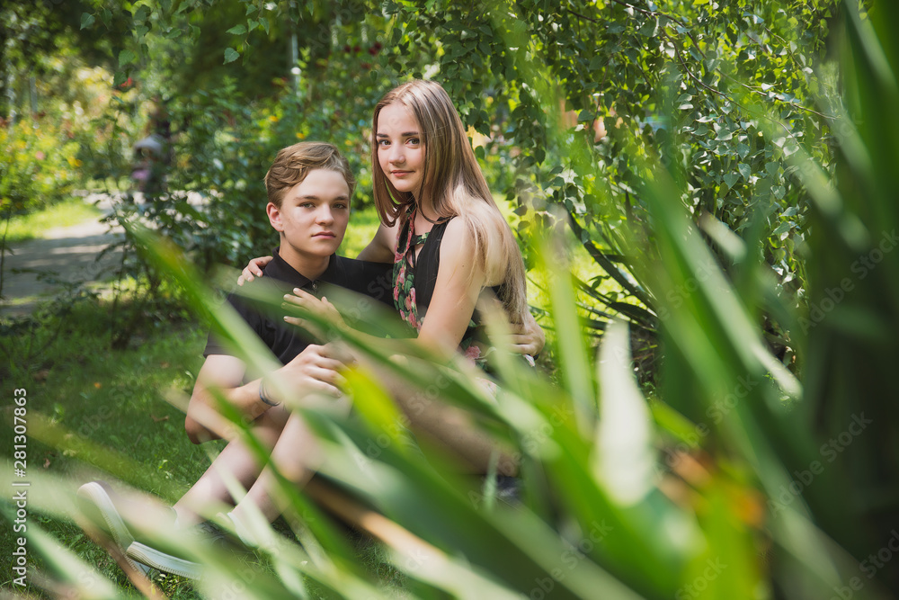 Obraz premium A couple of teenagers in love hugs and poses against the background of flowering trees and shrubs. Young guy and girl on the background of a blooming Park