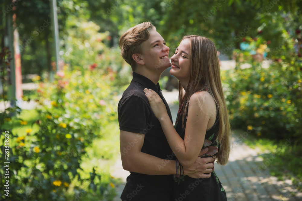 A couple of teenagers in love hugs and poses against the background of flowering trees and shrubs. Young guy and girl on the background of a blooming Park A couple of teenagers in love hugs and poses against the background of flowering trees and shrubs. Young guy and girl on the background of a blooming Park