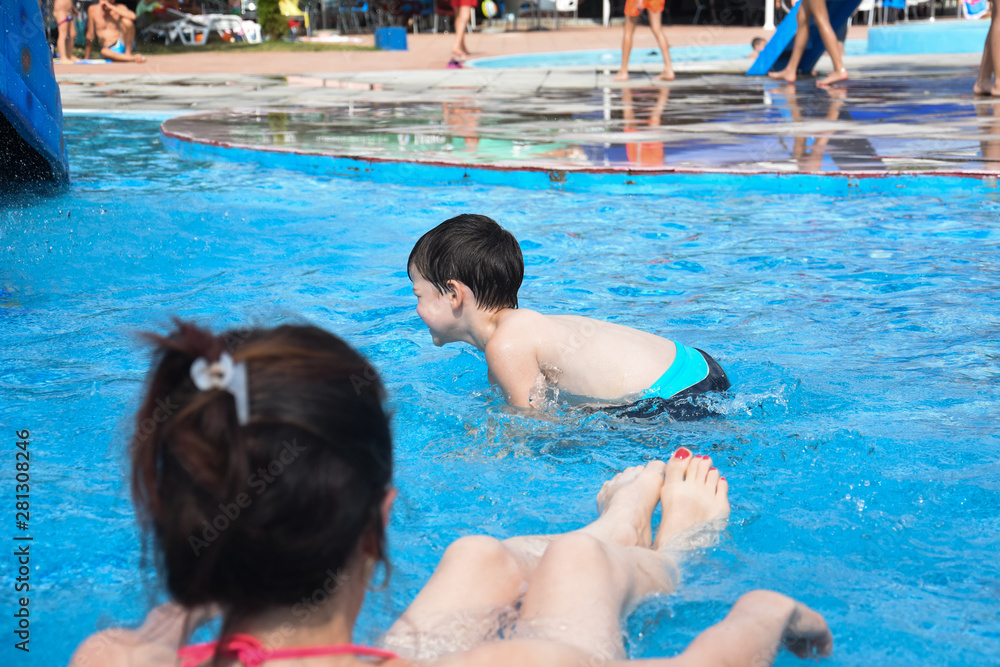 40 Years old Mom play with son in a pool. Cheerful child splashing in the swimming pool with  his mother