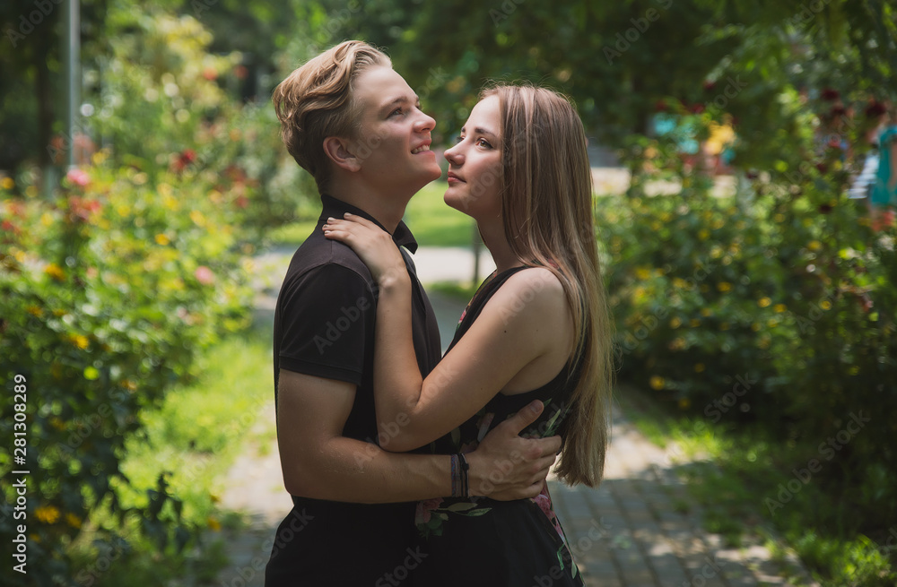 A couple of teenagers in love hugs and poses against the background of flowering trees and shrubs. Young guy and girl on the background of a blooming Park A couple of teenagers in love hugs and poses against the background of flowering trees and shrubs. Young guy and girl on the background of a blooming Park