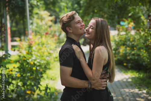 A couple of teenagers in love hugs and poses against the background of flowering trees and shrubs. Young guy and girl on the background of a blooming Park