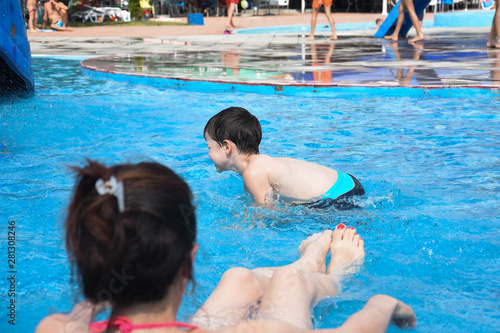 40 Years old Mom play with son in a pool. Cheerful child splashing in the swimming pool with  his mother © Ivan