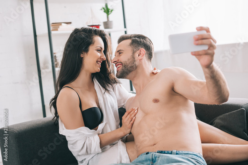 handsome man and sexy woman in shirt and bra looking at each other and taking selfie