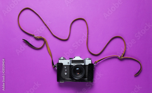 Vintage retro film camera in leather cover with strap on purple background. Top view
