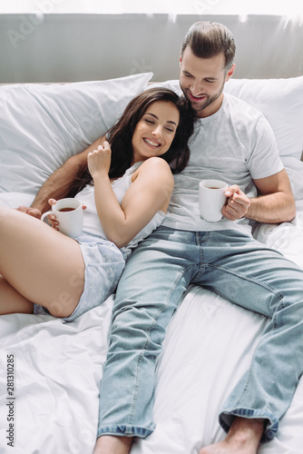 attractive and brunette woman and man lying on bed and hugging