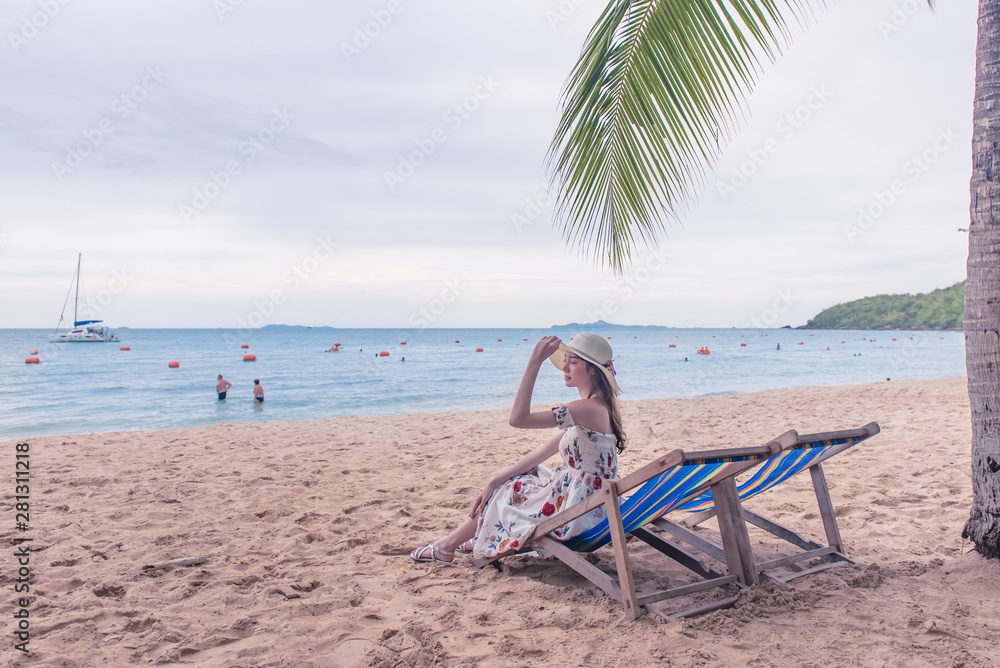 Summer beach vacation concept, Happy young Asian woman with hat relaxing on beach chair and raised hands up.