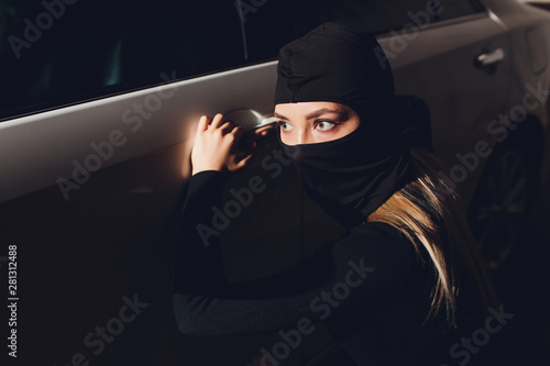 Fototapeta Masked robber woman car The thief is levering the lock at the door car robbery