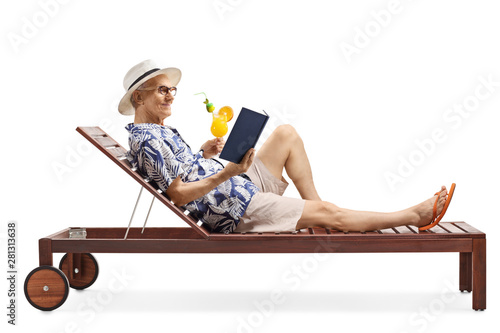 Elderly male tourist on a lounge bed reading a book and holding a cocktail © Ljupco Smokovski
