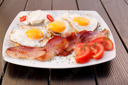 Healthy bacon fried egg on toast bread breakfast on plate , fresh tomatoes and cheese on plate , wood background.