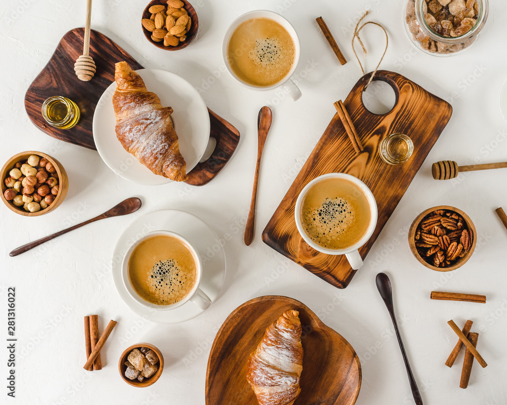 Continental breakfast captured from above (top view, flat lay). Сoffee and croissants, nuts, cinnamon, pecan, hazelnut, honey, almonds, cutting board, wooden, spoon, lump sugar.