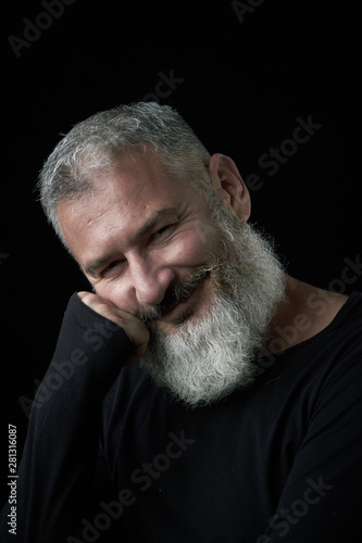 Portrait of a smiling brutal gray-haired man with a gray-haired lush beard on a black background, selective focus