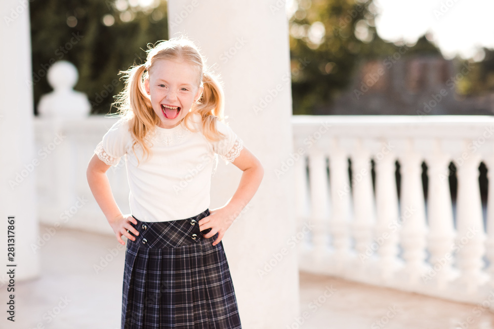 Laughing kid girl 5-6 year old wearing checkered skirt outdoors. Back to school. Pre schooler.