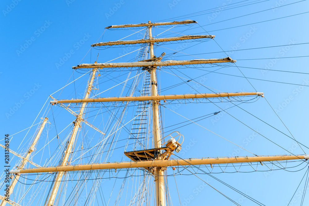 Bottom view of the mast, sail yards with the lowered sails and rigging of a sailing ship against a clear sky. Bottom view of the mast, sail yards with the lowered sails and rigging of a sailing ship against a clear sky.