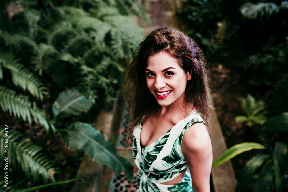 portrait of beautiful blonde young woman smiling at sunset in a green house surrounded by tropical plants. Happiness and lifestyle concept portrait of beautiful blonde young woman smiling at sunset in a green house surrounded by tropical plants. Happiness and lifestyle concept