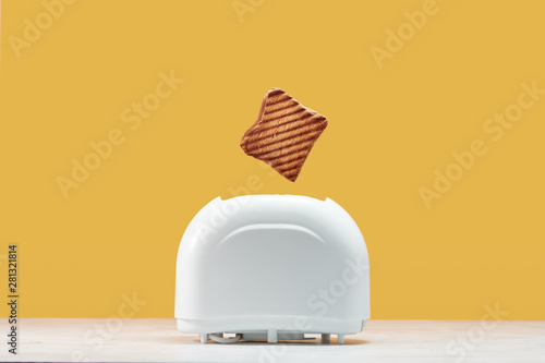 Roasted toast bread popping up of toaster with yellow wall photo