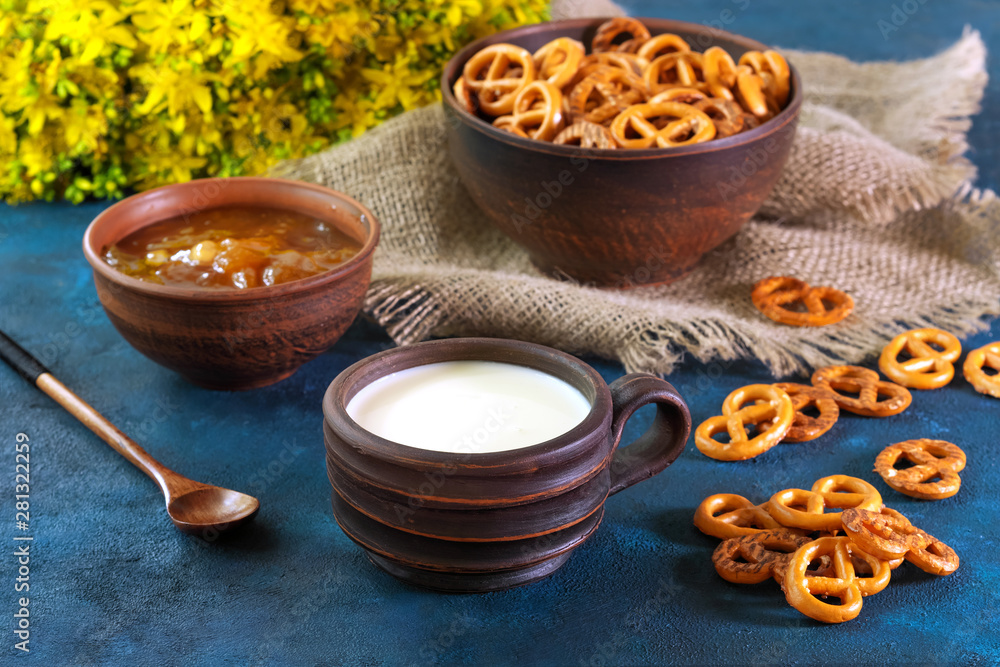 Still life in a rustic style. Crumbled pretzels on a textural background with milk in a clay cup, with apricot jam in a clay plate. Still life in a rustic style. Crumbled pretzels on a textural background with milk in a clay cup, with apricot jam in a clay plate.