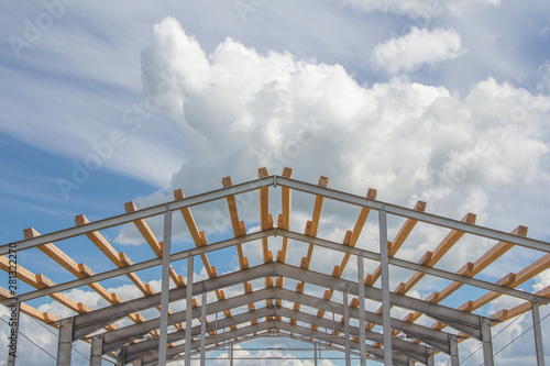 Wooden beams on the metal frame of the building against the blue sky. Roofing during the construction of the hangar.