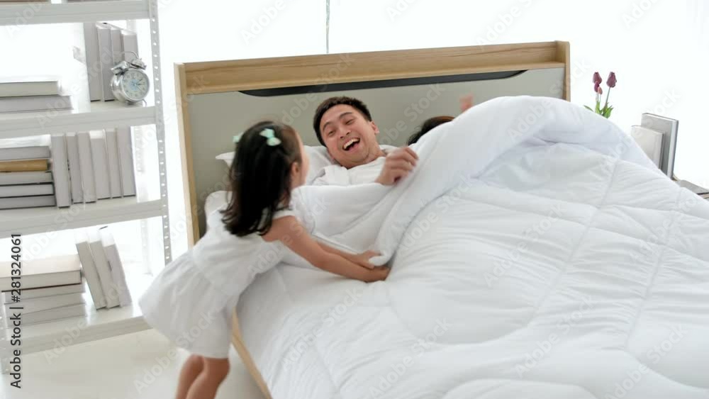 Asian family happy spending time together in the house. Father, mother and daughter aged three playing hide and seek in the blanket on the bed. Asian family happy spending time together in the house. Father, mother and daughter aged three playing hide and seek in the blanket on the bed.