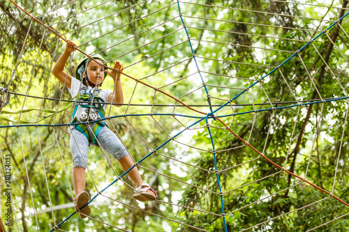 Adorable little girl enjoying her time in climbing adventure park on warm and sunny summer day. Summer activities for young kids. Child having fun on school vacations.