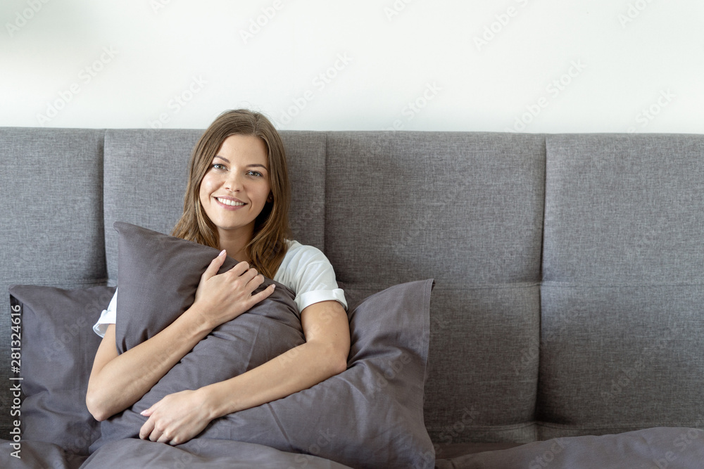 Young adult woman sitting on bed and hugging pillow Young adult woman sitting on bed and hugging pillow