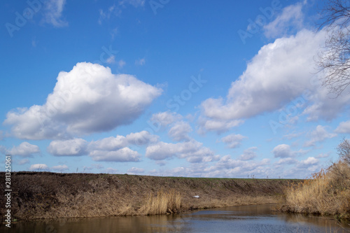 Fototapeta Naklejka Na Ścianę i Meble -  View of the river, shore and blue sky with white cumulus clouds.