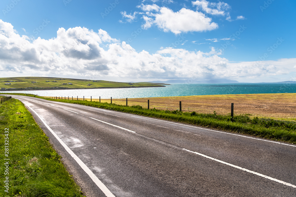 Deserted road running alongside a beautiful bay on a sunny summer day. Orkney Islands, Scotland, UK.