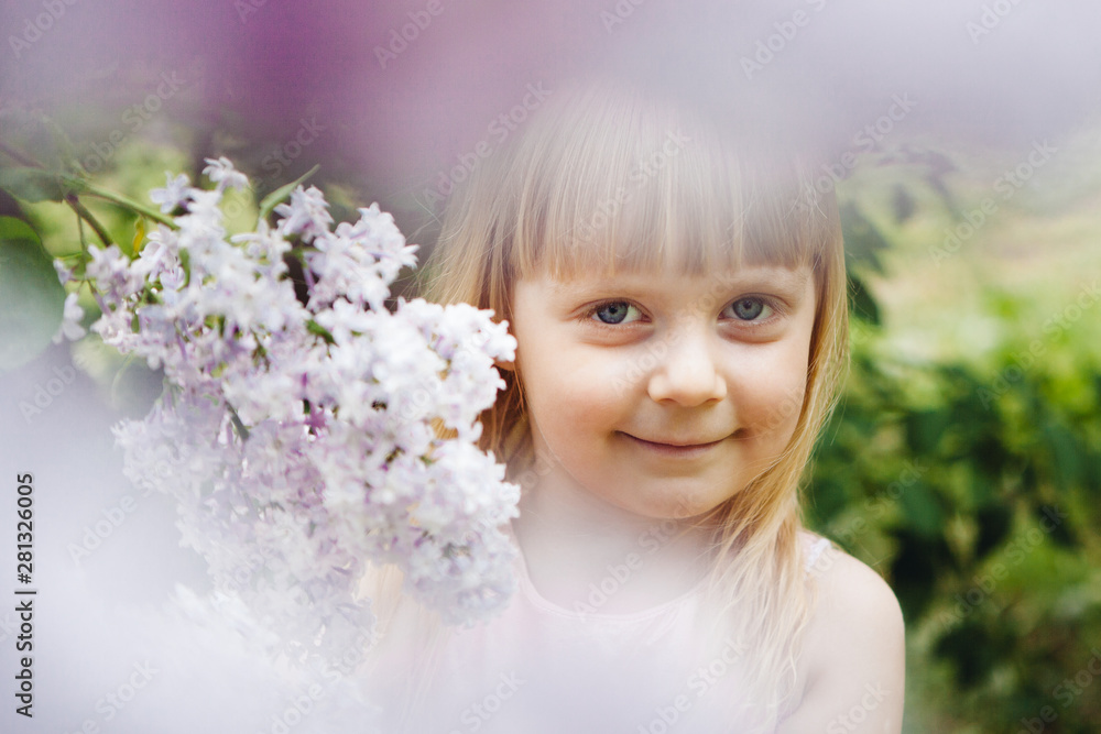 Beautiful little girl smiling with lilac flowers around, portrait of child Beautiful little girl smiling with lilac flowers around, portrait of child