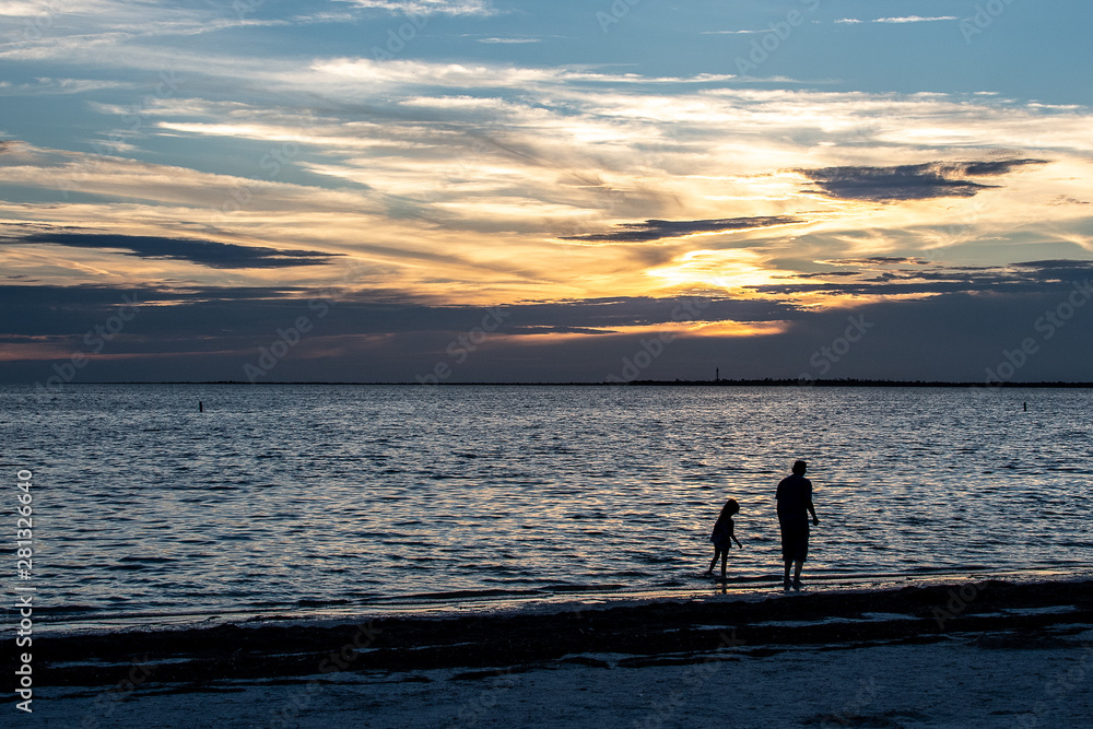 Parent and small child have a summer stroll on the beach as the sun sets