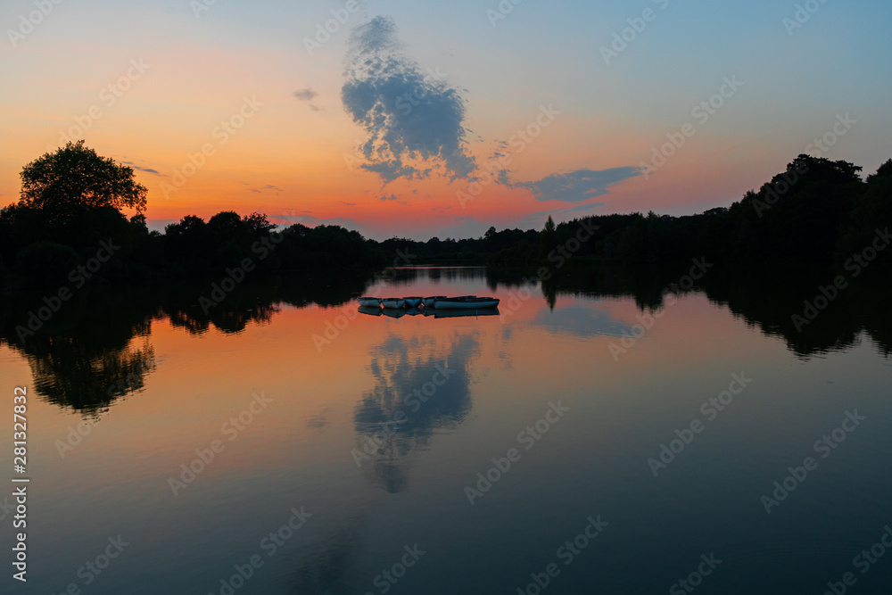 tranquil, twilight sunset shot over lake with reflections of sky and clouds in water and rowing boats to centre of lake